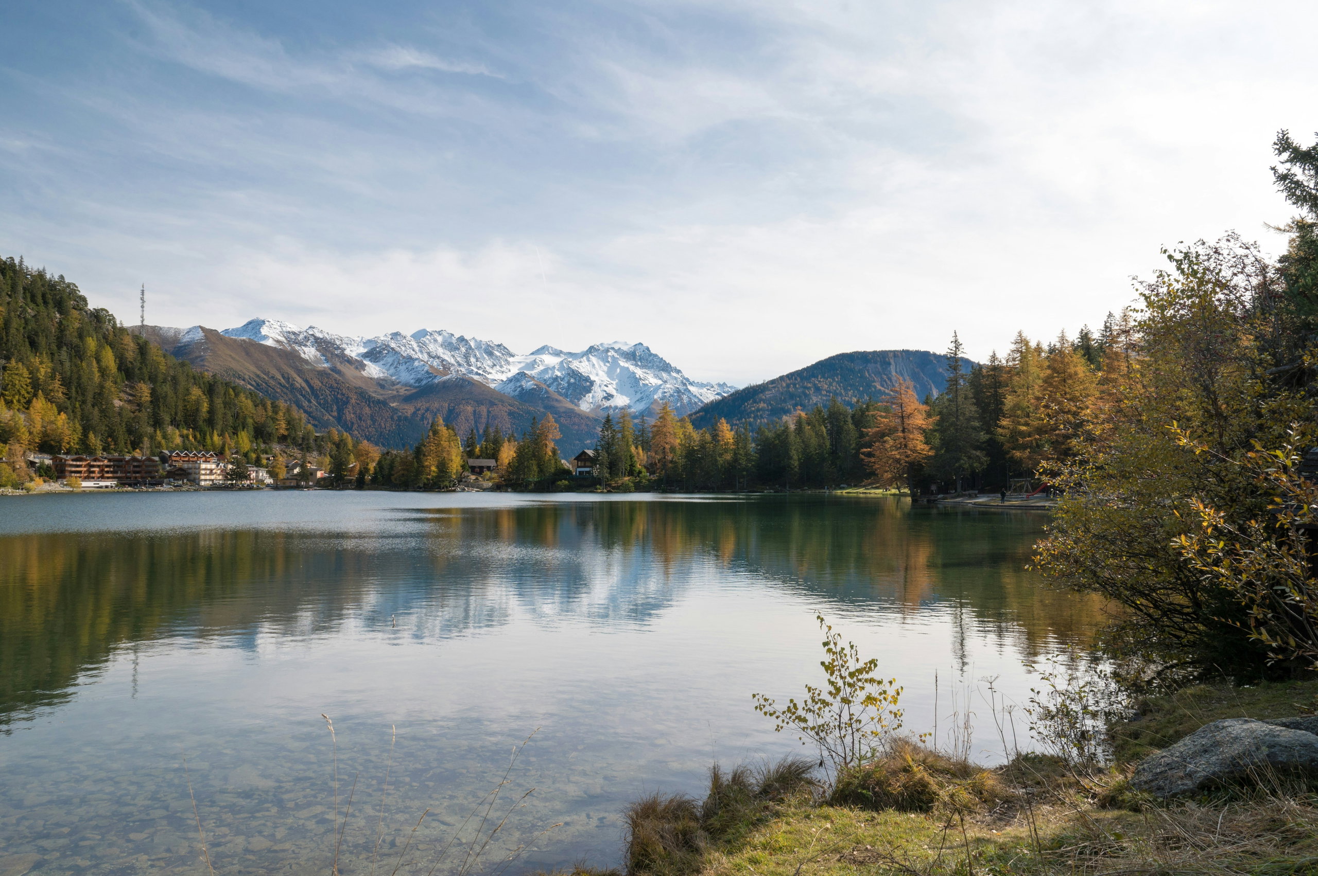 The still waters of Lac de Champex in the Swiss Valais reflecting golden autumn larches and the snow-dusted peaks of the Mont Blanc massif.