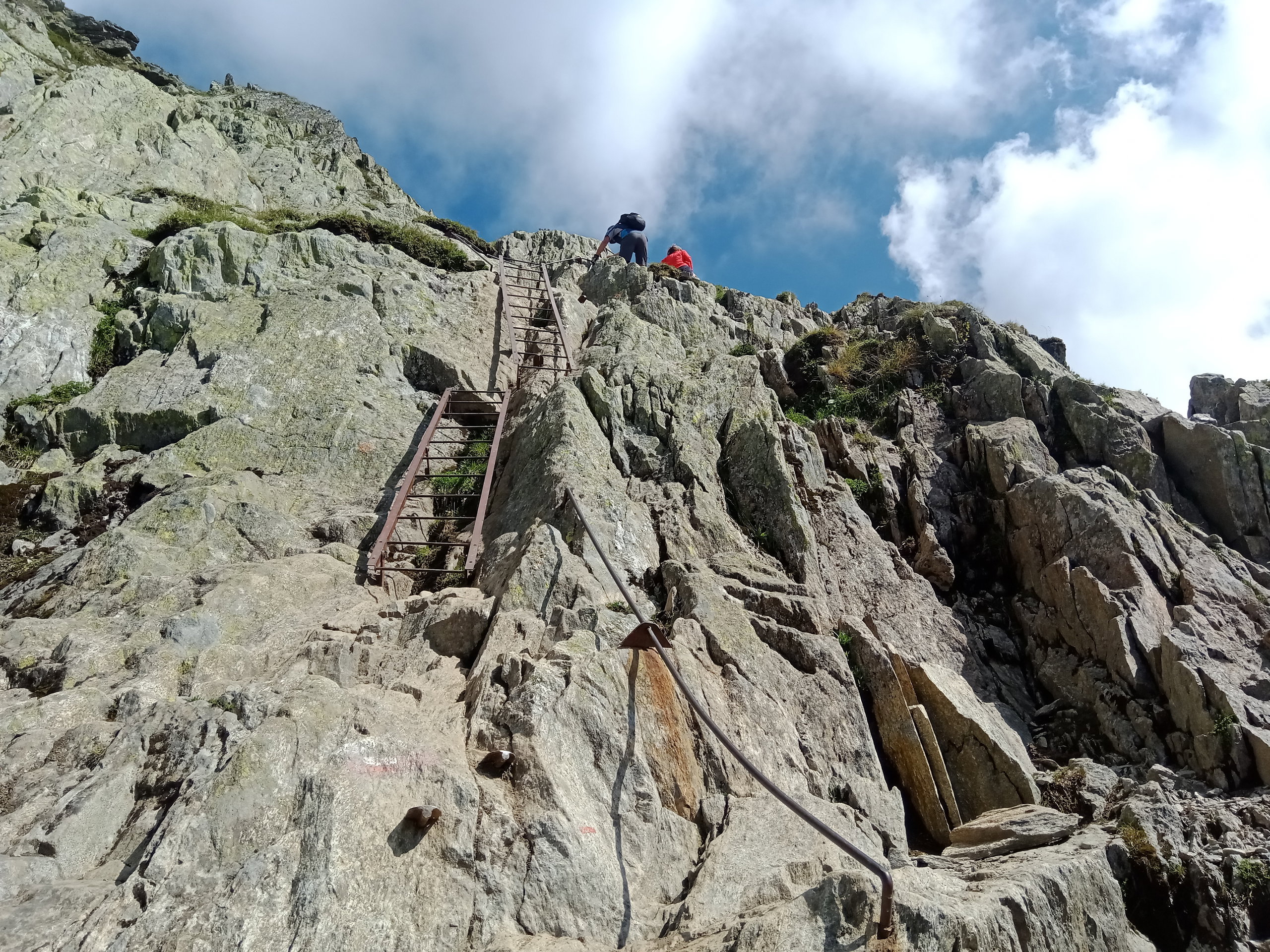 Hikers ascending the steep metal ladders and handrails bolted to the rocky cliffs of Le Brévent.