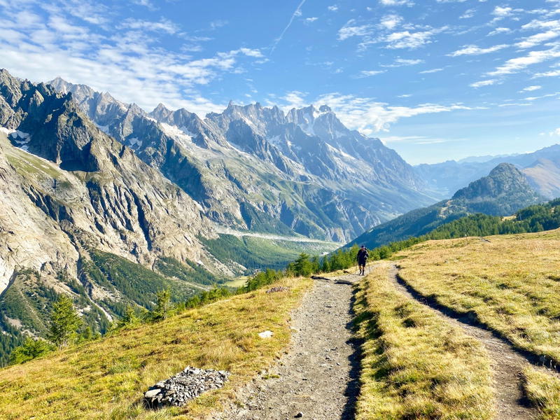 Hiker on a winding trail in the Italian Val Ferret facing the Grandes Jorasses massif, Aosta Valley.