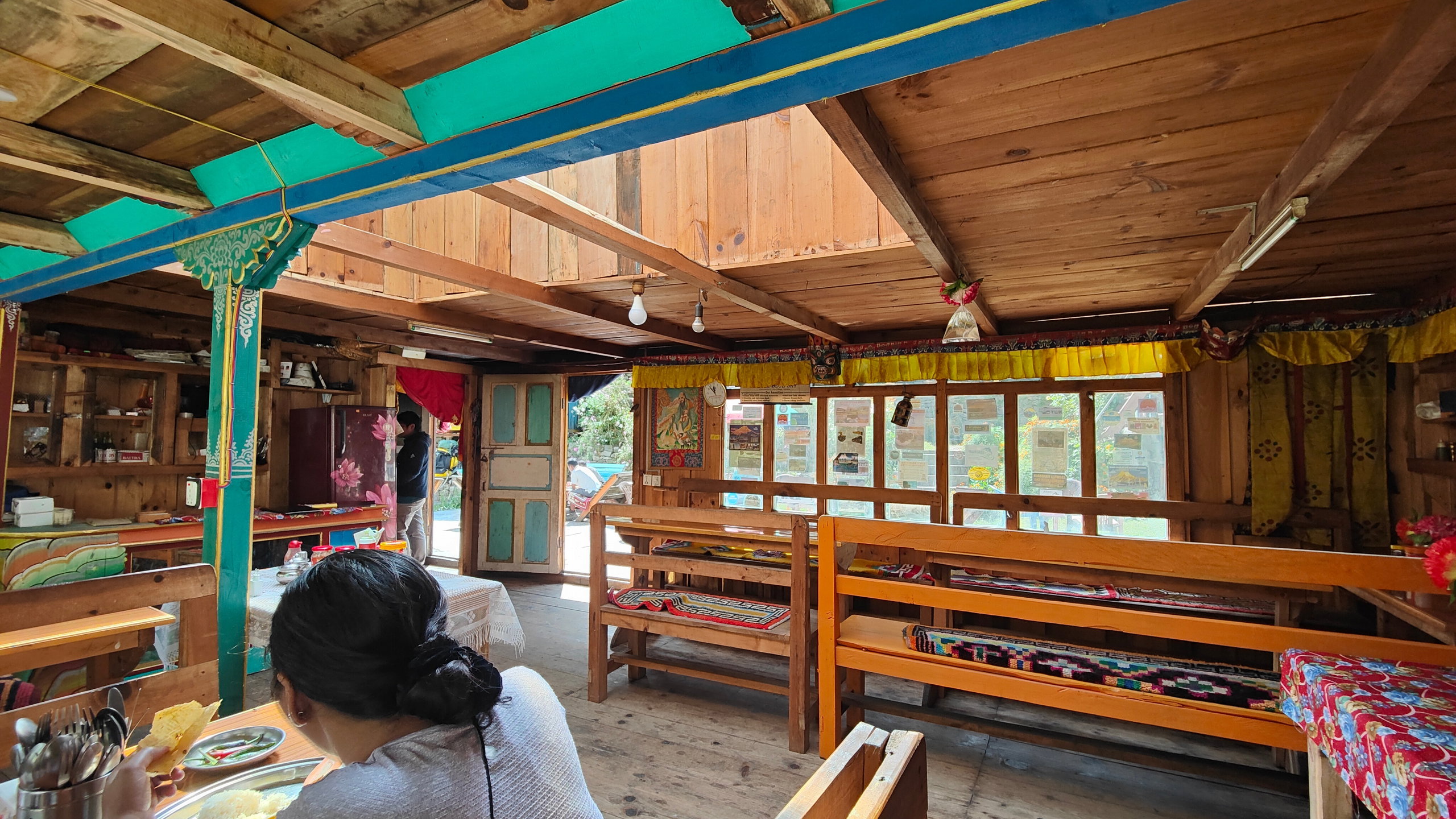 A colourful dining room with exposed timber and a woman sitting with her back to the camera.