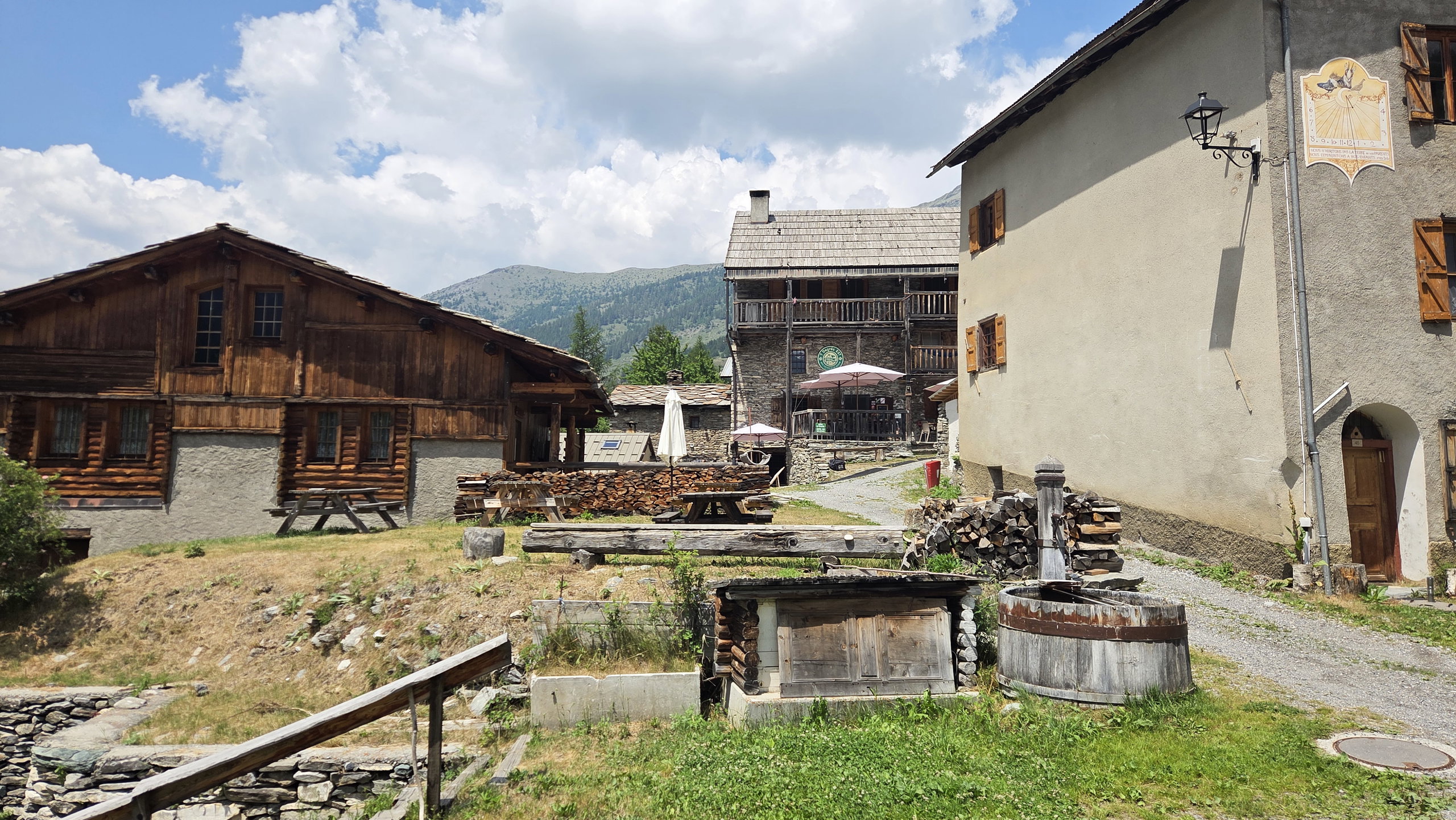 Traditional houses in the hamlet of L'Echalp beneath steep green and rocky mountains