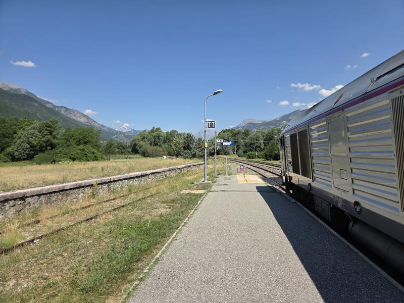Night train standing at Mont-Dauphin-Guillestre station under a blue sky.
