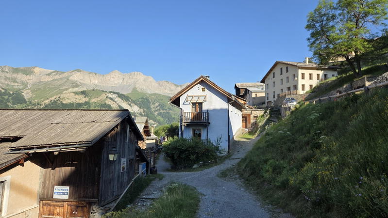 A narrow path through Saint Véran with wooden houses and high mountains beyond.