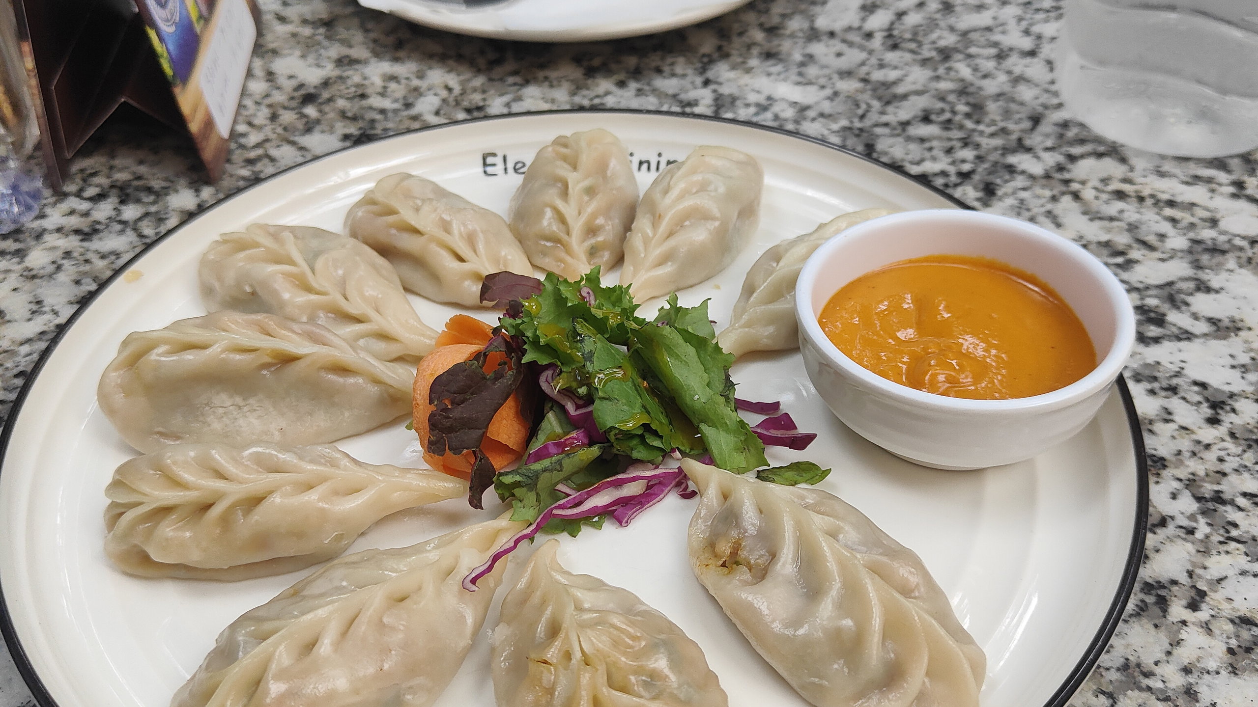 A plate of momos arranged in a circle with orange sauce.