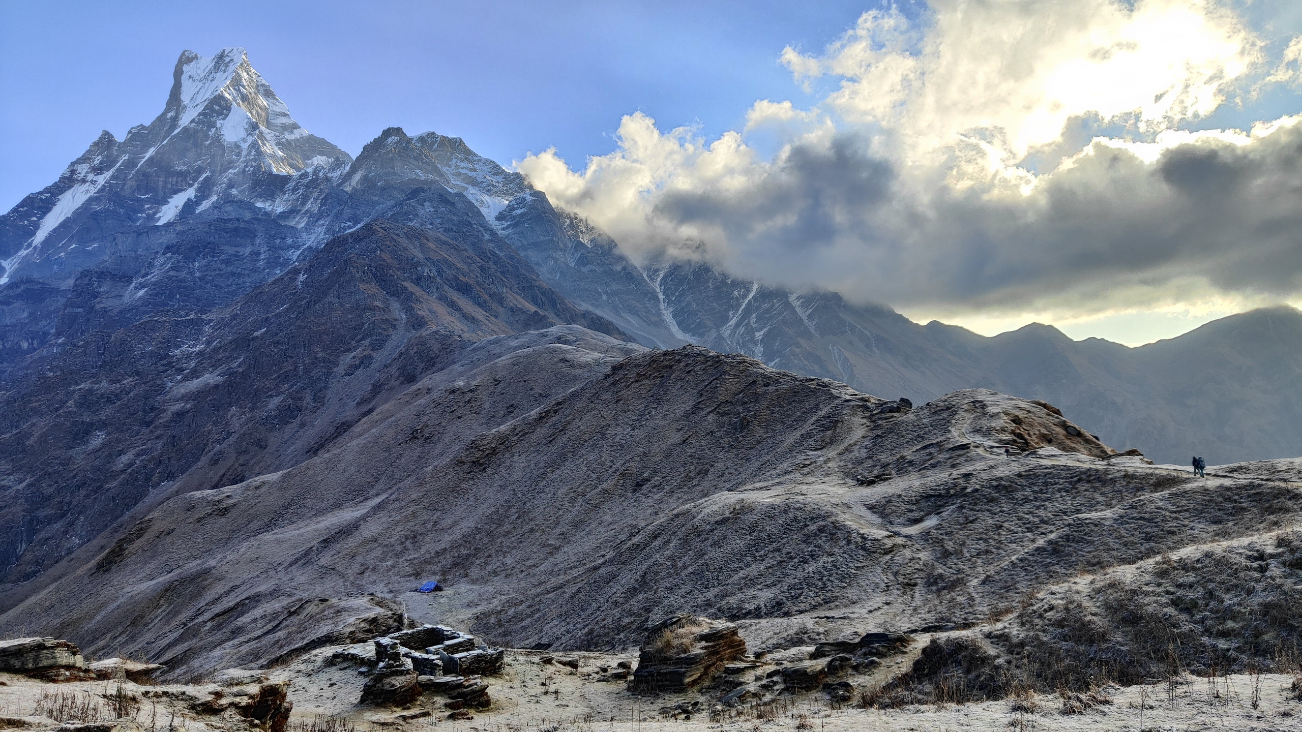 A frost-covered rocky ridge and Machhapuchhre rising above the clouds
