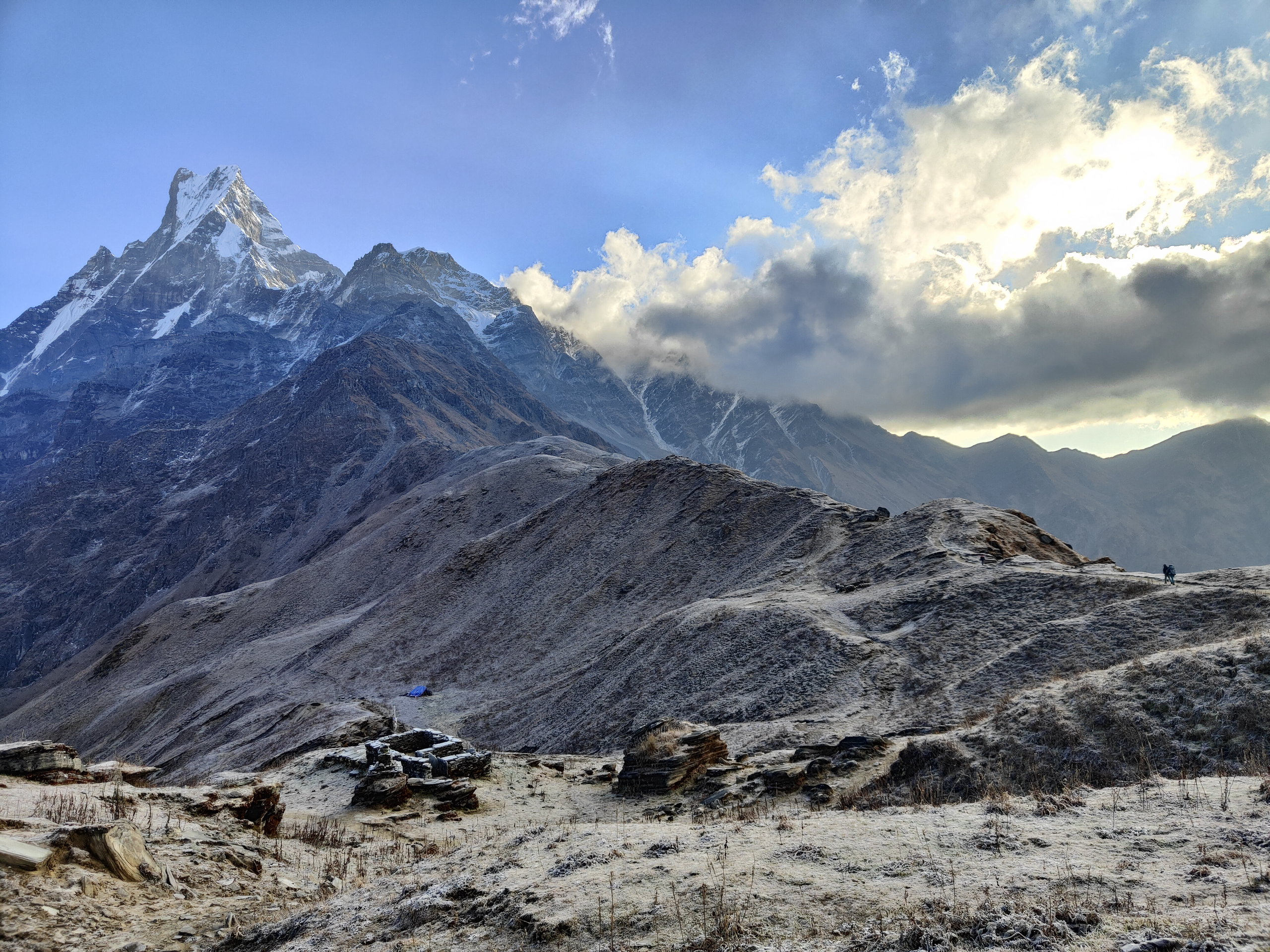 A frost-covered rocky ridge and Machhapuchhre rising above the clouds