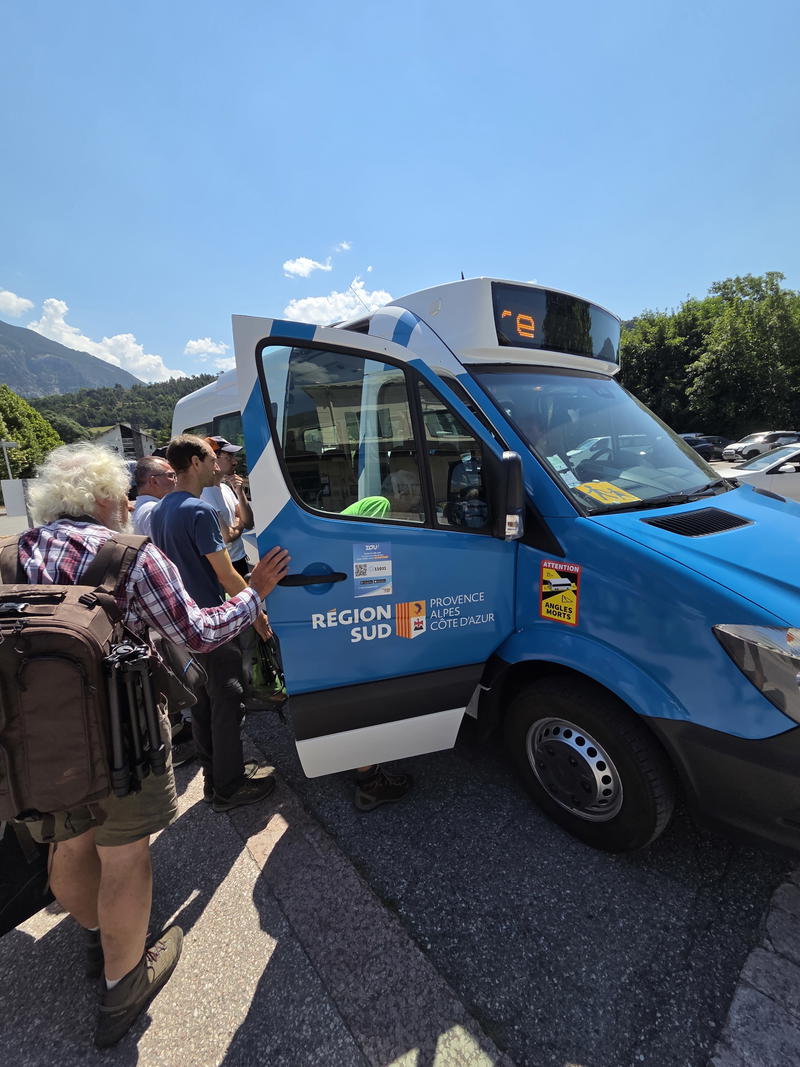 Hikers boarding a blue regional shuttle bus with their luggage.