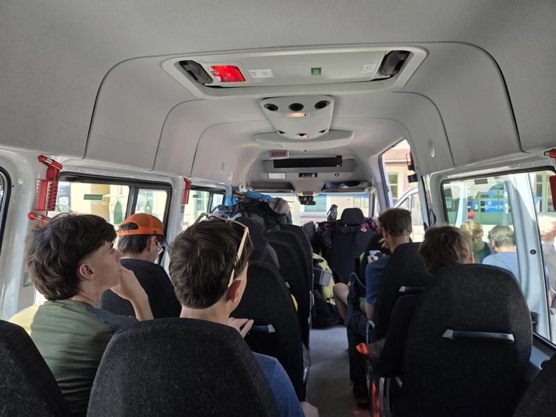 Hikers seated inside a shuttle bus with backpacks filling the aisle.