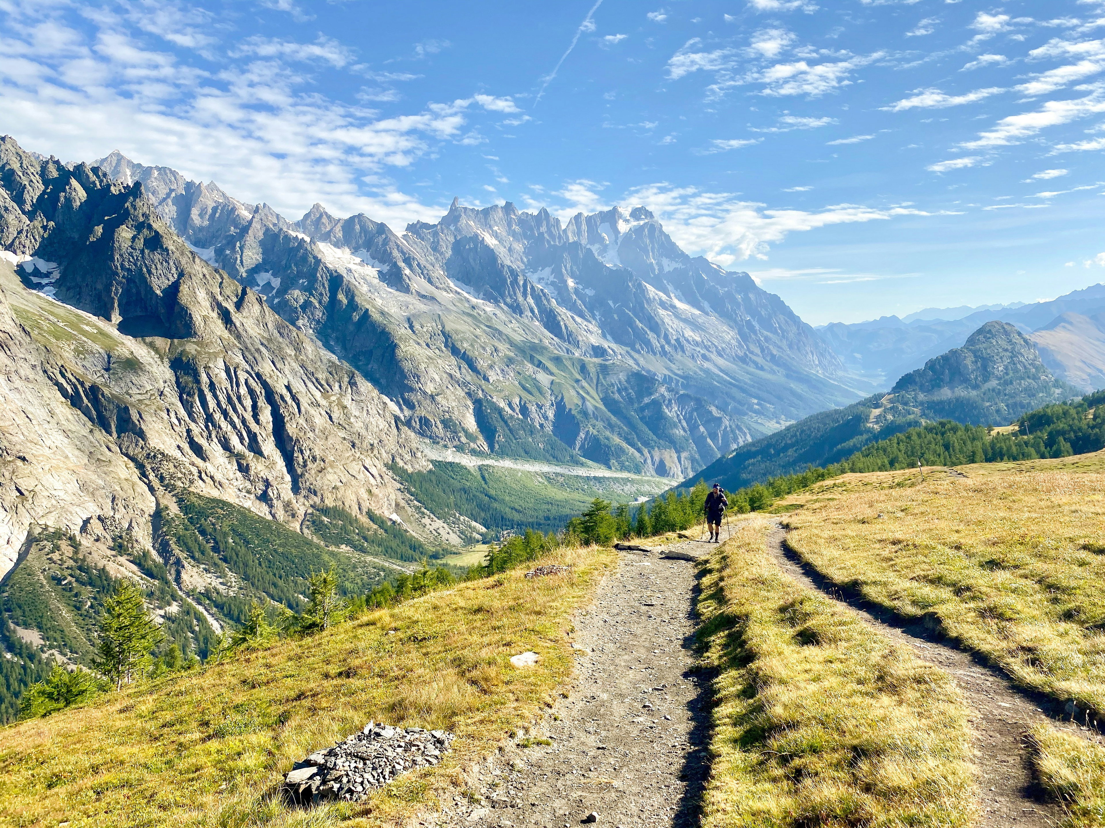 Hiker on a winding trail in the Italian Val Ferret facing the Grandes Jorasses massif, Aosta Valley.